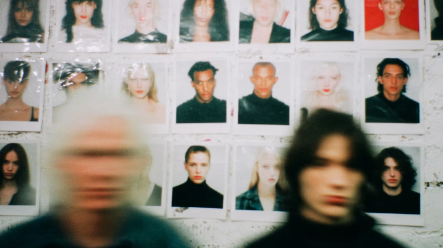 Blurred figures passing in front of a casting wall covered in model polaroids